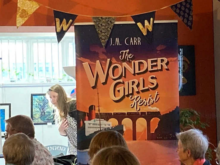 Vertical banner displaying the cover of The Wonder Girls Resist and the author's adult daughter popping out from behind it!