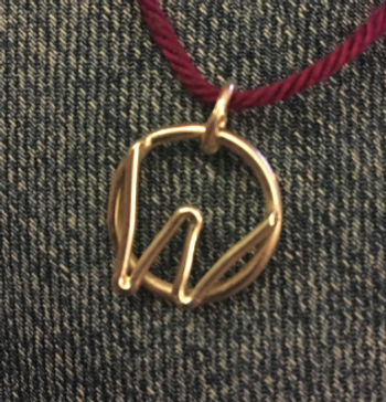 looks like gold but is actually a silver W in a circle  as a pendant on a  purple string.