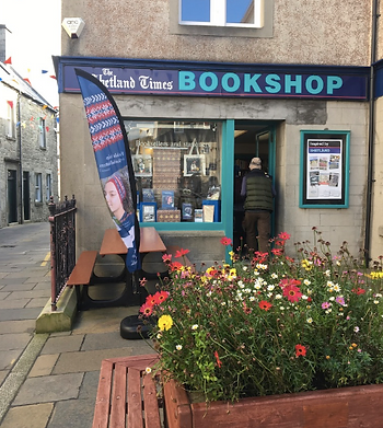 Customer entering The Shetland Times Bookshop, a raised bed of flowers in the foreground